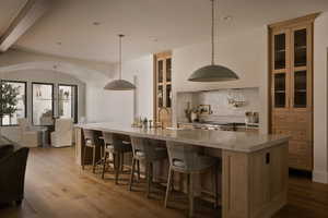 Dual tone kitchen with glass insert cabinets, a breakfast bar, dark wood-style flooring, light stone counters, and a large island with sink