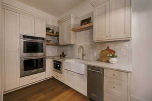 Kitchen with stainless steel appliances, open shelves, light stone counters, dark wood-style floors, and white cabinetry