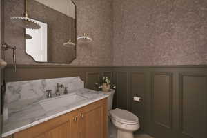 Bathroom featuring wallpapered walls, vanity, a wainscoted wall, and a decorative wall