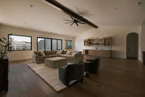 Living area featuring arched walkways, dark wood-style flooring, a ceiling fan, beamed ceiling, and beverage cooler