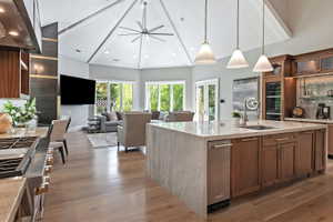 Kitchen with glass insert cabinets, light stone countertops, range hood, wood finish cabinets, and open floor plan