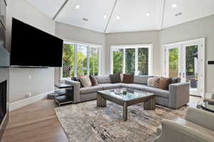 Living room featuring french doors, light wood finished floors, a custom gas fireplace, and opens to the expansive patios and pool.
