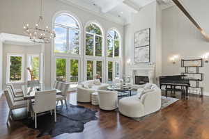 Living room featuring ornamental molding, a  cast stone fireplace with raised hearth, dark wood-style flooring, coffered ceiling, large dining area, and soaring 2-story Palladium windows!