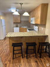 Kitchen featuring a breakfast bar area, white appliances, a peninsula, light wood-style flooring, and tasteful backsplash