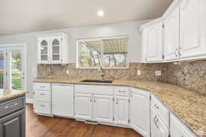 Kitchen featuring light stone countertops, white dishwasher, dark wood-style flooring, glass insert cabinets, and recessed lighting