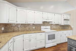 Kitchen with white appliances, light stone countertops, vaulted ceiling, parquet floors, and tasteful backsplash