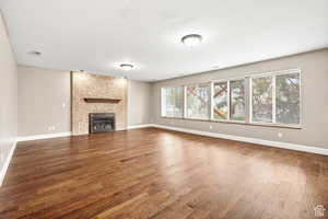 Unfurnished living room with dark wood-style flooring and a brick fireplace
