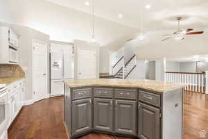 Kitchen with two tone cabinetry, a kitchen island, white appliances, ceiling fan, and vaulted ceiling