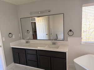 Full bath featuring double vanity, a freestanding tub, and light marble finish floors