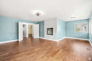 Unfurnished living room with dark wood-style flooring and a brick fireplace