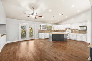 Kitchen with a center island, tasteful backsplash, white appliances, lofted ceiling, and white cabinets