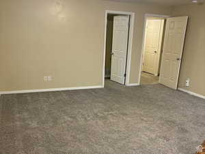 Unfurnished bedroom featuring dark colored carpet and baseboards