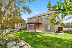 Rear view of house featuring a patio area, a lawn, stucco siding, a chimney, and a wooden deck