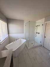 Bathroom featuring a stall shower, a freestanding bath, light marble finish flooring, vanity, and a wainscoted wall