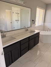 Full bath featuring a soaking tub, double vanity, light marble finish flooring, and a shower stall