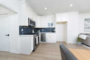 Kitchen with stainless steel appliances, light wood-type flooring, white cabinets, backsplash, and recessed lighting