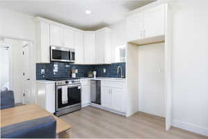 Kitchen featuring stainless steel appliances, light wood-type flooring, white cabinets, tasteful backsplash, and recessed lighting