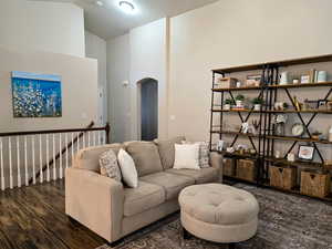 Living area with arched walkways, dark wood-style flooring, and vaulted ceiling