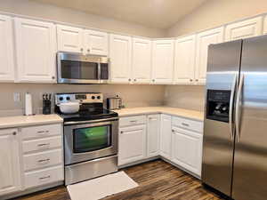 Kitchen with stainless steel appliances, white cabinetry, light countertops, dark wood-type flooring, and lofted ceiling