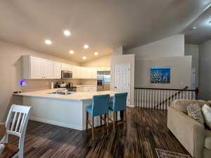 Kitchen featuring light countertops, lofted ceiling, a peninsula, stainless steel appliances, and white cabinetry