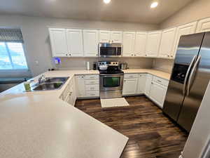 Kitchen with stainless steel appliances, white cabinetry, light countertops, a peninsula, and dark wood-style flooring