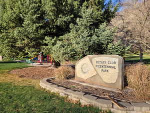 Community sign featuring a yard and view of wooded area