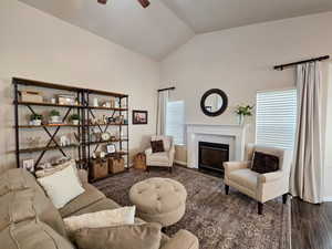 Living area with vaulted ceiling, a fireplace, a ceiling fan, and dark wood-type flooring