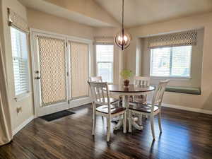 Dining area featuring vaulted ceiling, dark wood-style flooring, and a chandelier