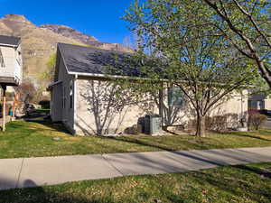 View of side of property with stucco siding, a lawn, a mountain view, and a shingled roof