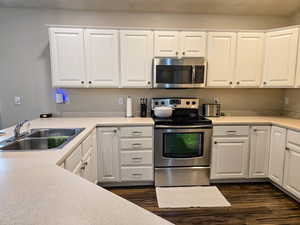 Kitchen featuring stainless steel appliances, white cabinetry, light countertops, and dark wood-style flooring