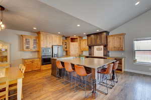 Kitchen with light wood-style floors, a spacious island, glass fronted cabinets, stainless steel appliances, and a breakfast bar area