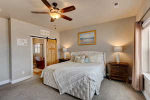 Master Bedroom featuring a barn door, ensuite bath, a ceiling fan, and light colored carpet