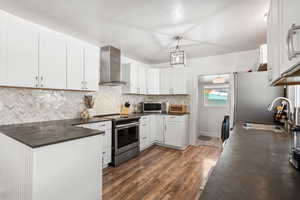 Kitchen with dark countertops, stainless steel appliances, white cabinets, dark wood-type flooring, and hanging light fixtures