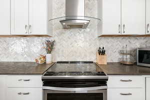 Kitchen with stainless steel appliances, exhaust hood, white cabinetry, and dark stone countertops