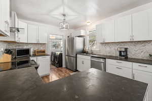Kitchen featuring white cabinets, stainless steel appliances, wood finished floors, washer and dryer, and decorative backsplash