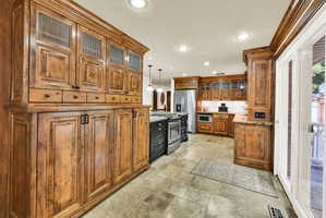 Kitchen featuring glass fronted cabinets, wood finish cabinets, decorative light fixtures, stainless steel appliances, and light stone counters