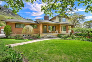 View of front of property with brick siding, a front yard, covered porch, a chimney, and a shingled roof