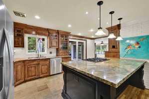 Dual tone kitchen with light stone countertops, stainless steel appliances, a kitchen island, glass insert cabinets, and hanging light fixtures