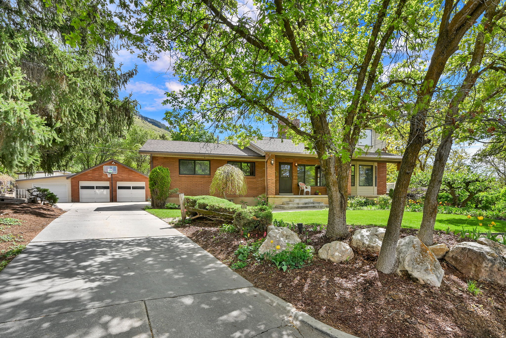Single story home featuring an outdoor structure, brick siding, a detached garage, covered porch, and a front yard
