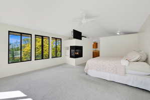 Carpeted bedroom featuring lofted ceiling, a multi sided fireplace, and ceiling fan