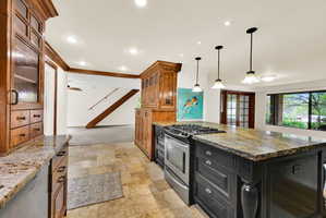 Two tone kitchen with glass fronted cabinets, stainless steel appliances, stone tile flooring, dark stone countertops, and ornamental molding