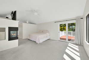 Bedroom with access to outside, light colored carpet, a multi sided fireplace, vaulted ceiling, and ceiling fan