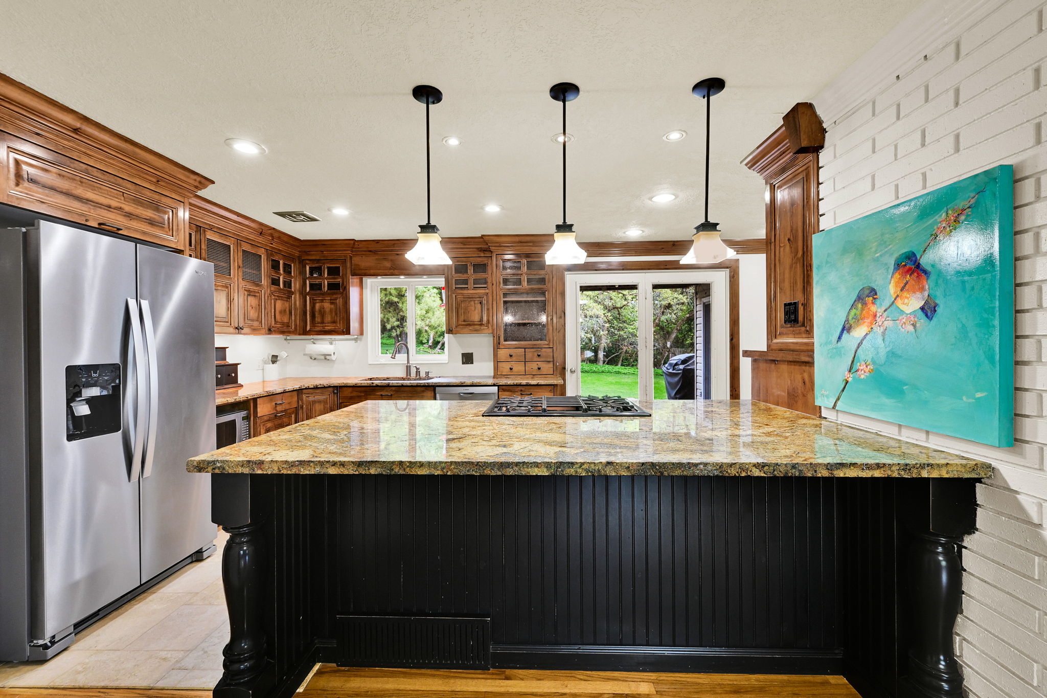 Kitchen featuring stainless steel appliances, light stone counters, pendant lighting, glass insert cabinets, and dark cabinetry