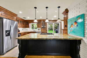Kitchen featuring stainless steel appliances, light stone counters, pendant lighting, glass insert cabinets, and dark cabinetry