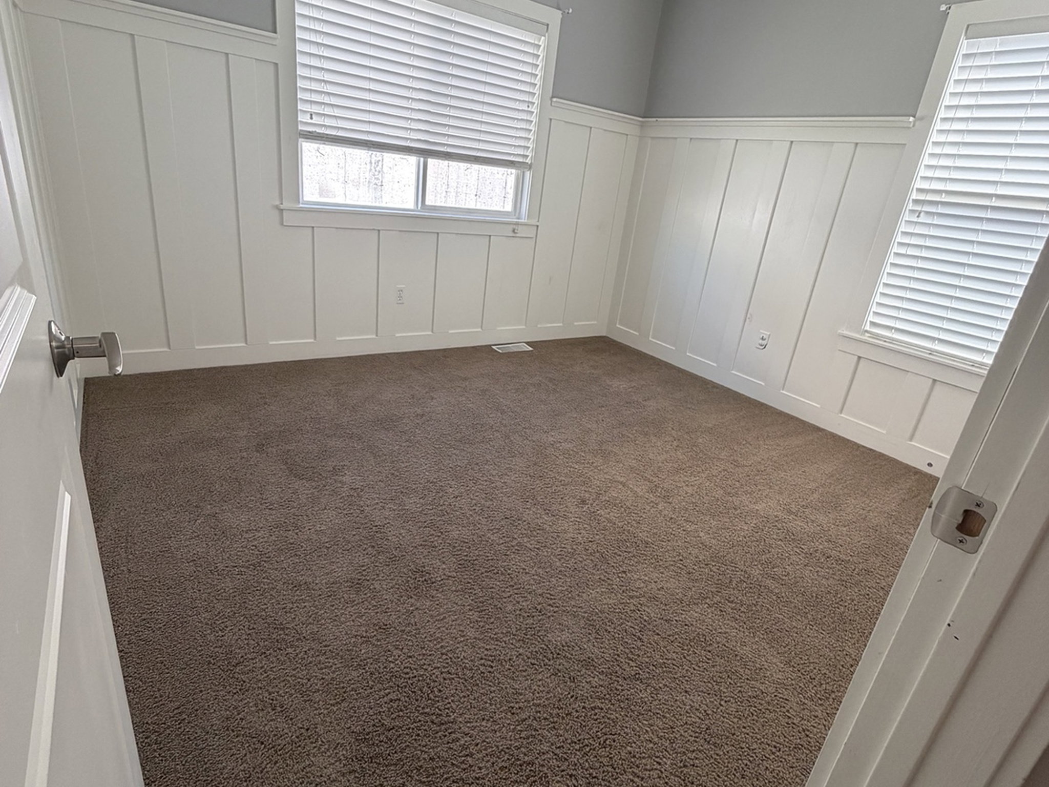 Unfurnished bedroom with a decorative wall, wainscoting, and dark colored carpet