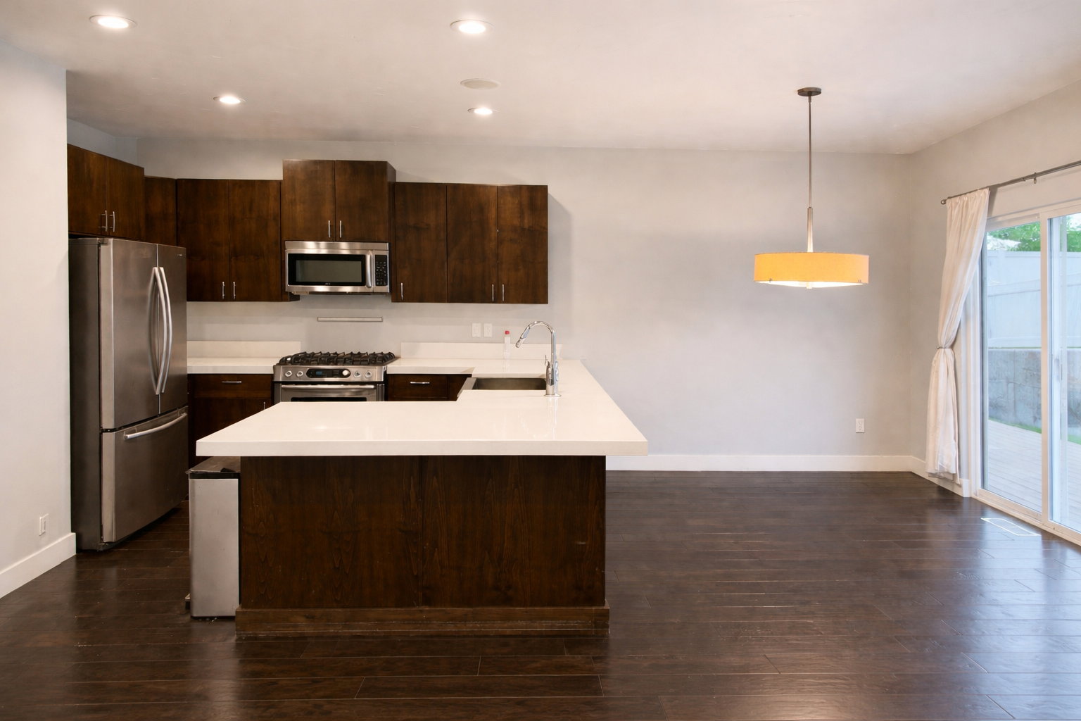 Kitchen featuring dark wood finish cabinetry, stainless steel appliances, dark wood-style floors, decorative light fixtures, and a peninsula