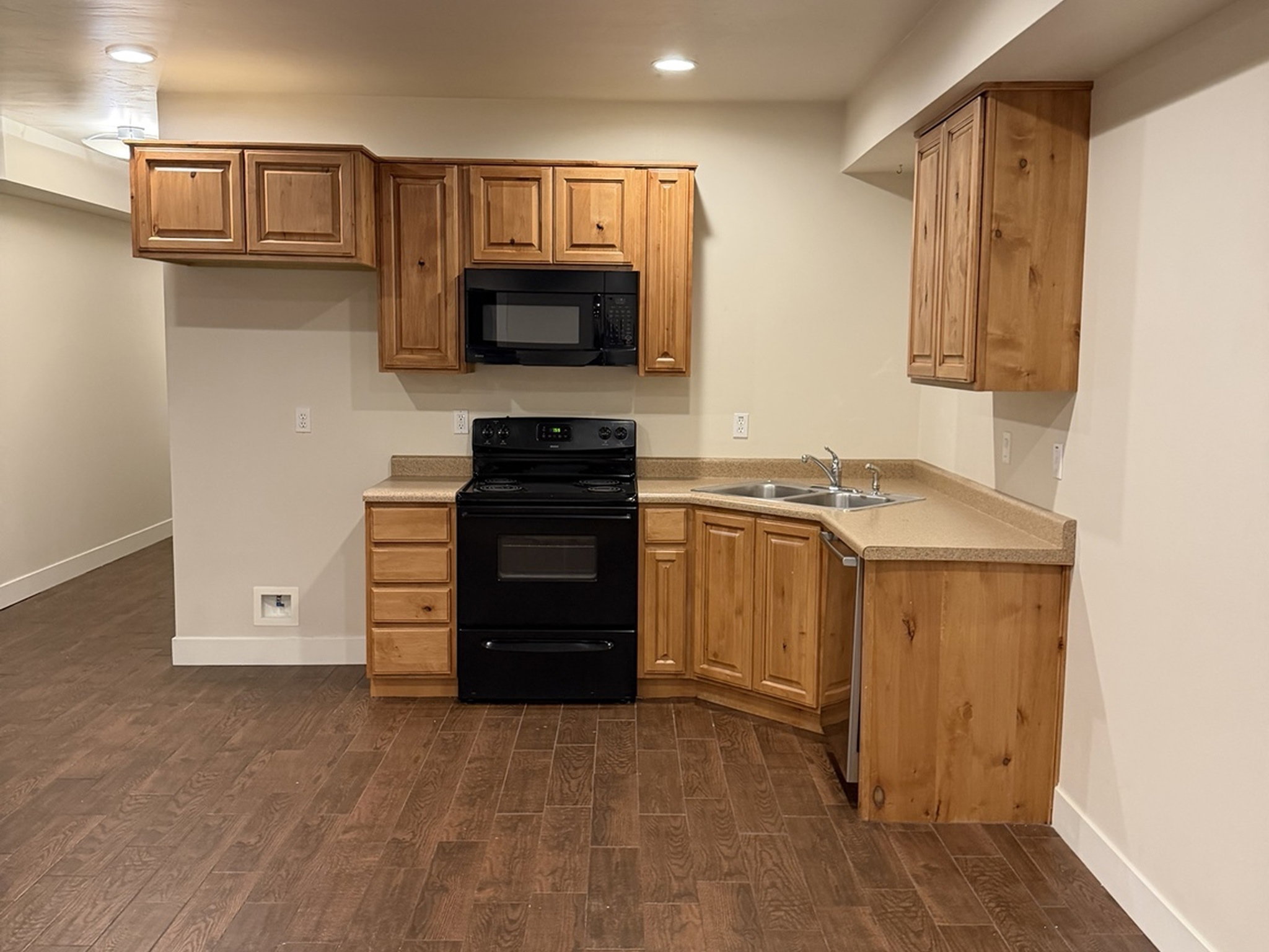 Kitchen with black appliances, dark wood-type flooring, light countertops, wood finish cabinets, and recessed lighting
