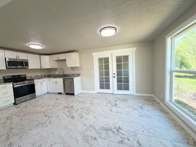 Kitchen with french doors leading to family room, stainless steel appliances, white cabinets, granite counters, tile flooring