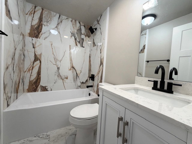 Full bath featuring vanity, tile surround and flooring, and a combined bath / shower.