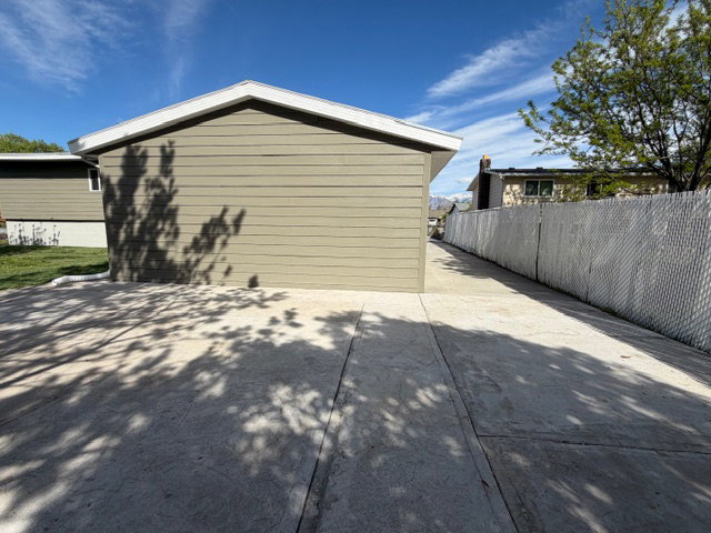 Rear of garage with additional patio or parking space, fully fenced yard and driveway with gate.